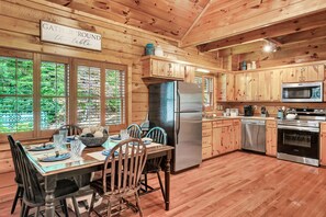 A wooden cabin interior with a dining table set for four, a stainless steel refrigerator, a microwave, and a dishwasher.