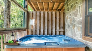 Un bain à remous doté d’un mur en pierre et d’une terrasse en bois, entouré de verdure.