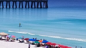 A beach with a pier extending into the water, umbrellas, and people relaxing on the sand.