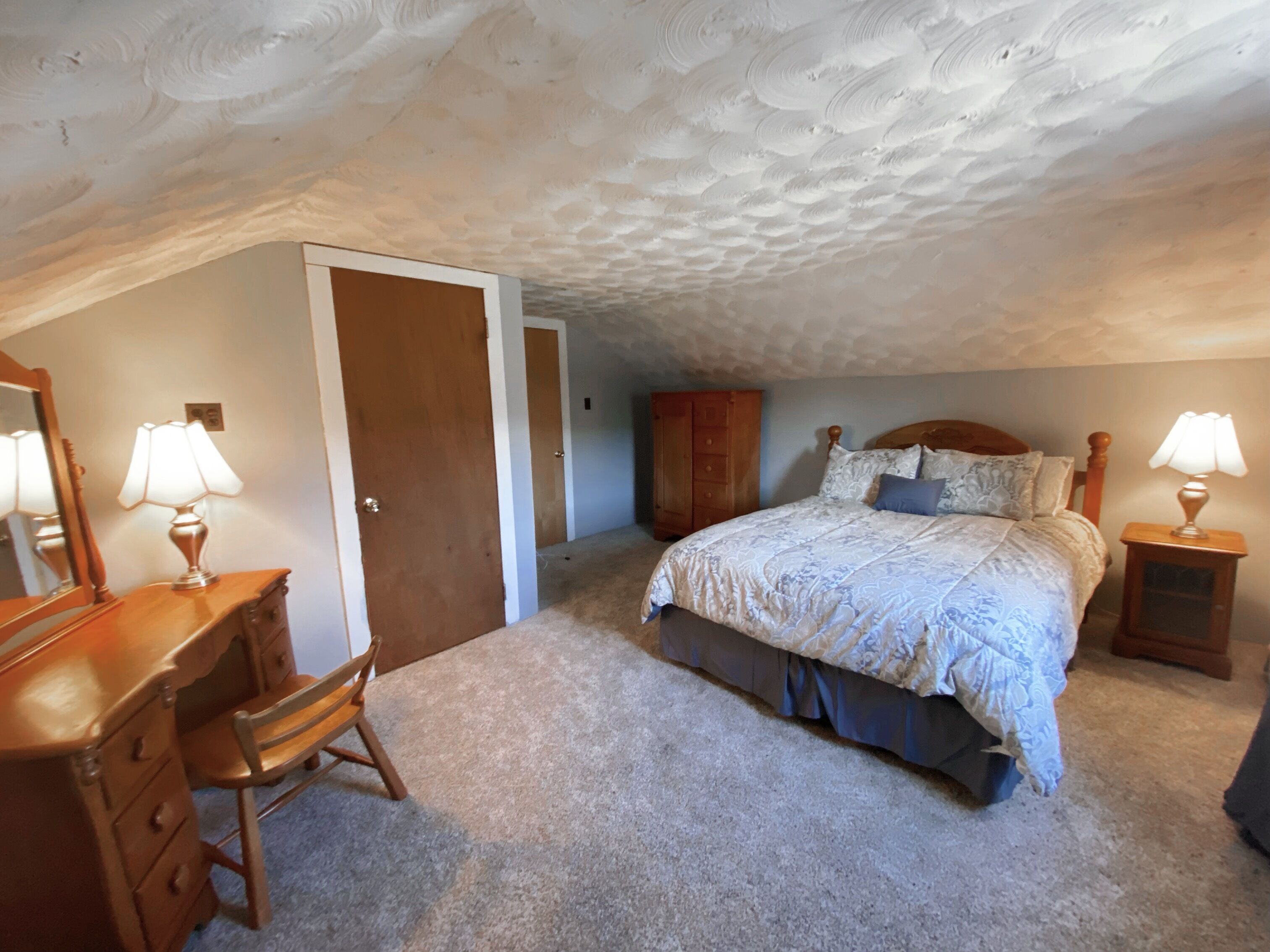 Une chambre à coucher comprenant un lit, une commode, une chaise, une armoire et un miroir.