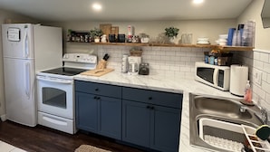 A compact kitchen with white appliances, dark blue cabinets, and a marble countertop. - Cute & cozy, close to downtown Boyne city!  (Boyne City)