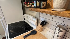 A kitchen with a white stove, a wooden cutting board, a black spatula, and a coffee mug rack. - Cute & cozy, close to downtown Boyne city!  (Boyne City)