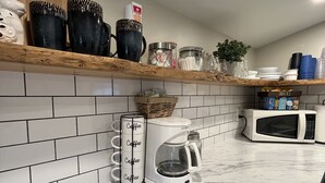 A kitchen with white subway tiles, a coffee maker, a microwave, and various kitchenware on shelves. - Cute & cozy, close to downtown Boyne city!  (Boyne City)