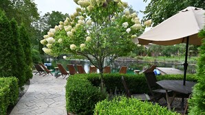 A stone pathway leading to outdoor seating with umbrellas, a pond, and lush greenery. - Scottland Yard Farm's - Upscale Rustic Garden House (Brooktondale)