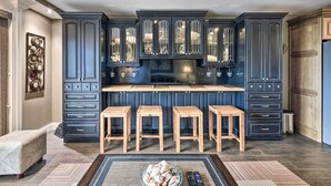 A modern kitchen with dark blue cabinetry, a central island with stools, and a bowl of fruit on the floor. - PCB Condo w/ 2 Outdoor Pools & Beach Access! (Panama City)