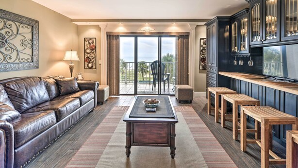 A living room with a leather sofa, a coffee table, and a kitchen area with bar stools. - PCB Condo w/ 2 Outdoor Pools & Beach Access! (Panama City)