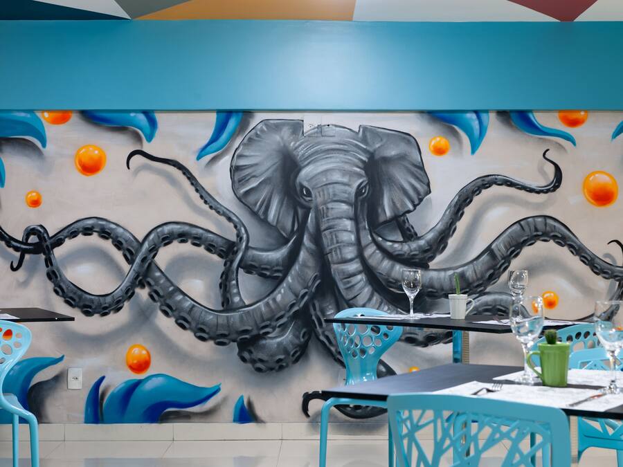 Interior de restaurante con un mural de elefante y pulpo, sillas azules y mesas dispuestas para comer.