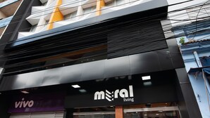 Un edificio moderno con un llamativo letrero que dice 'mral living', entrada de vidrio y plantas en macetas afuera.