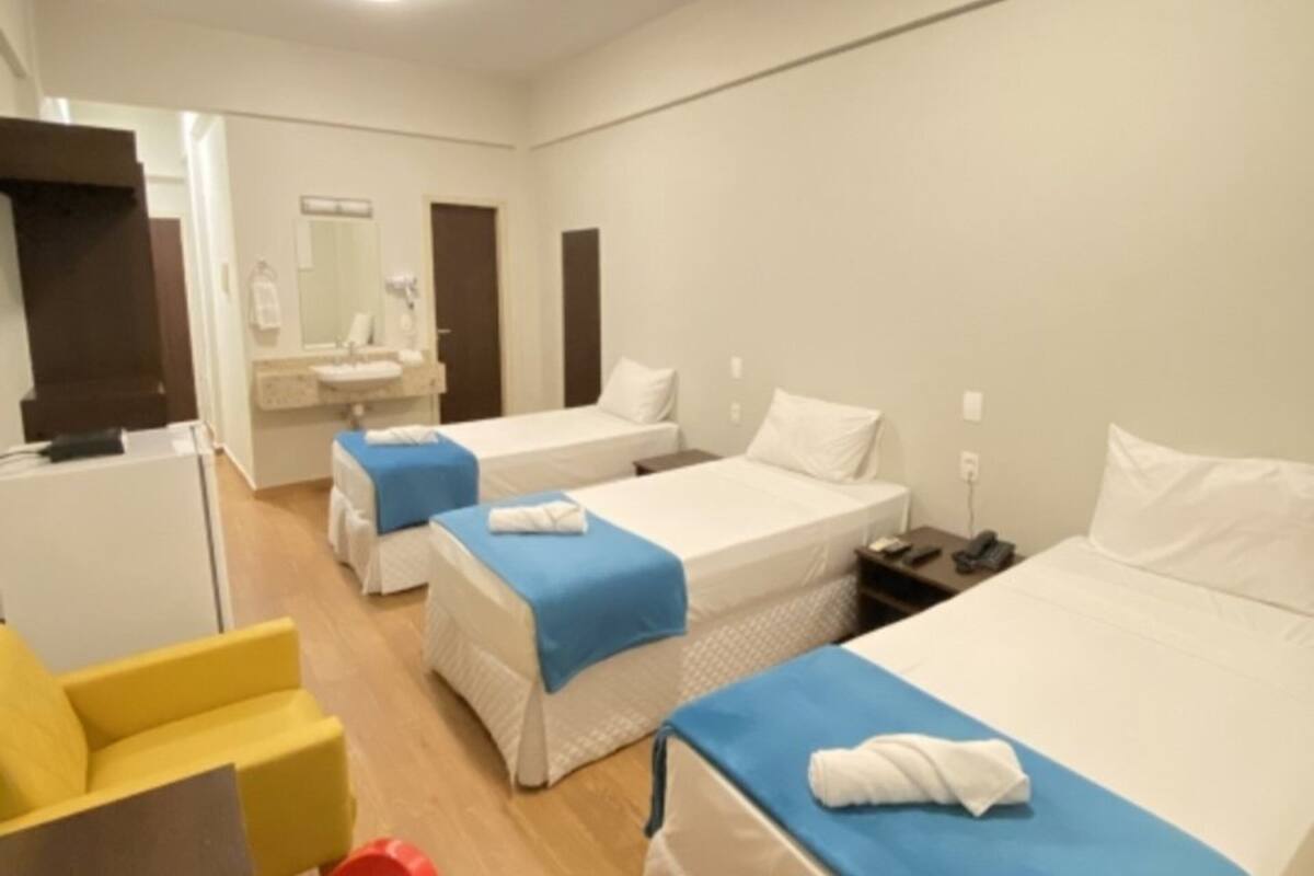A hotel room with two single beds, a small desk, a chair, and a bathroom with a mirror and sink.