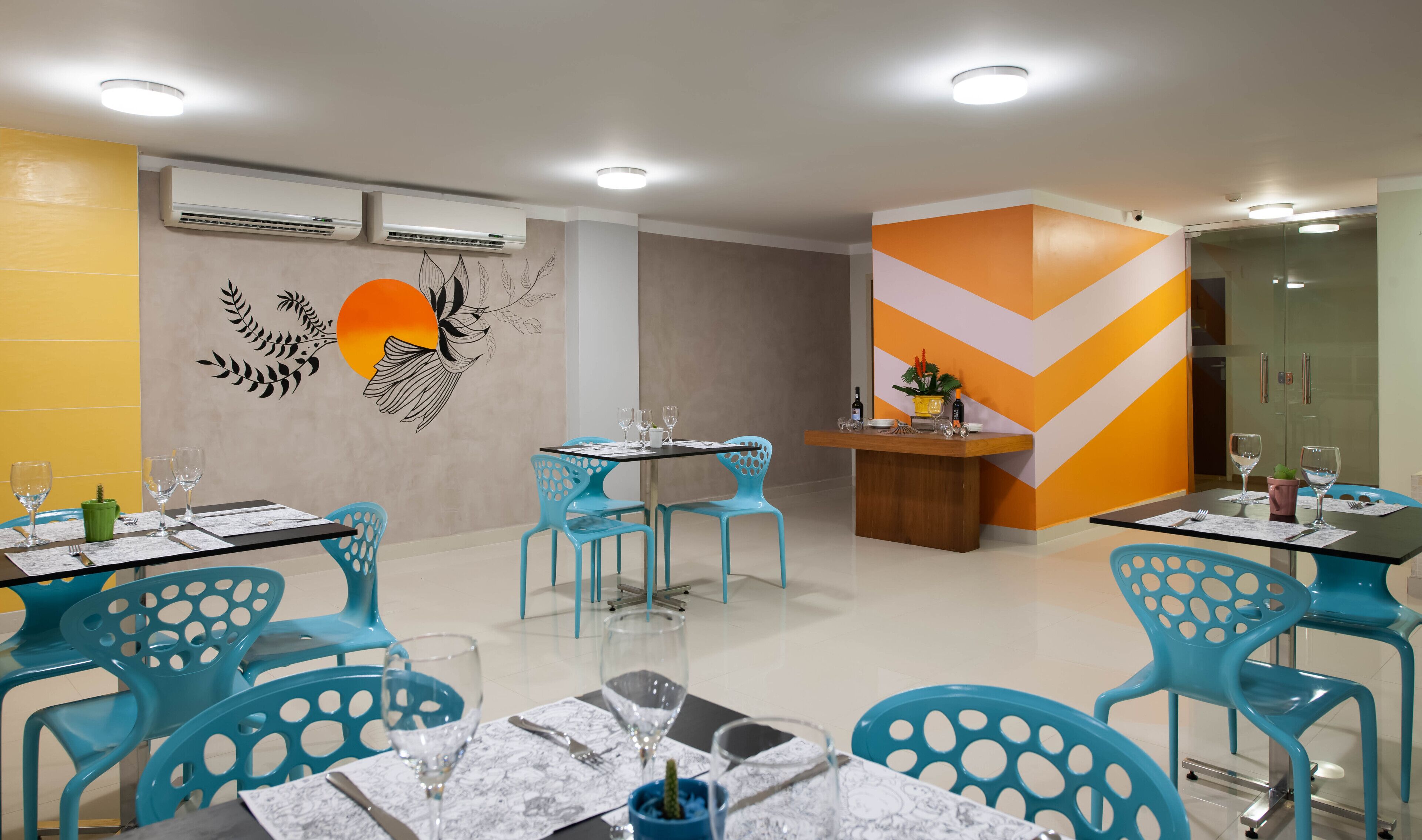 A dining area with blue chairs, tables set with wine glasses, and a decorative wall mural.