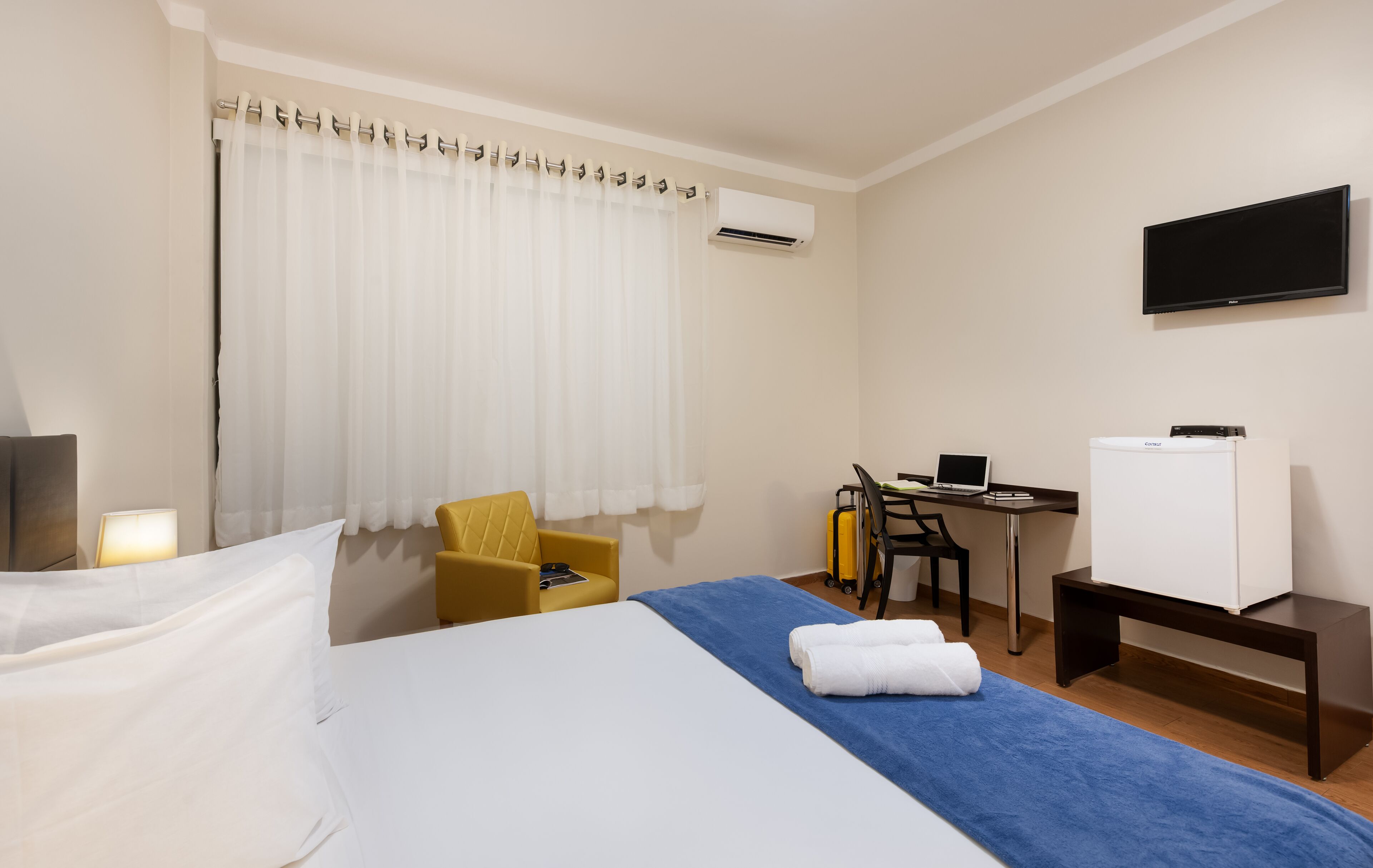 Habitación de hotel con cama, escritorio, silla, televisor y aire acondicionado.