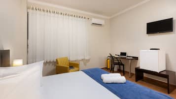 Habitación de hotel con cama, escritorio, silla, televisor y aire acondicionado.