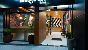 Una entrada de hotel moderna con fachada de vidrio, un mural y un letrero con plantas.