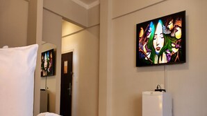 Una habitación de hotel con una cama, un televisor montado en la pared y un equipo de aire acondicionado blanco.