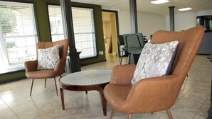 A room with two leather armchairs, a round table, and large windows.