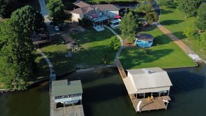 An aerial view of a residential area with a dock, a house with a covered porch, and a small blue structure.
