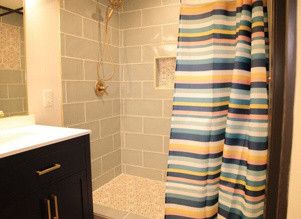 Un baño con ducha, paredes de azulejos, lavamanos y cortina de baño a rayas.