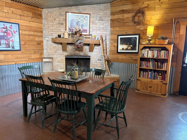 A dining area with a brick fireplace, wooden walls, a bookshelf, and a table with chairs. - Beautiful Country Shop Home/Cabin (Hartley)