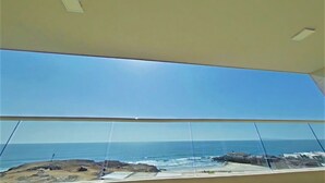 A room with a large window overlooking a rocky coastline and the sea. - Modern Ocean View  Condo with Private  Beach   (PLAYAS encantada, playa de Rosarito)