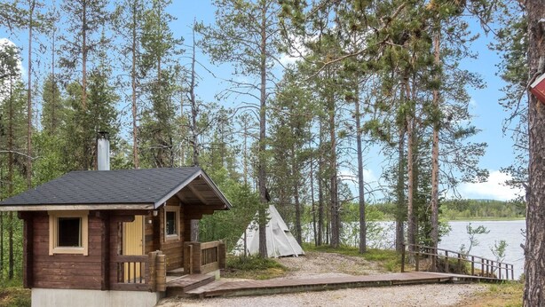 Uma cabana com varanda e vista para um lago rodeado por árvores.