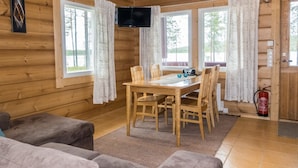 Interior de uma cabana de madeira com uma mesa de jantar, cadeiras, uma TV de tela plana e um extintor de incêndio.