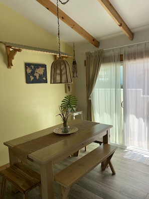 Une table à manger en bois, accompagnée d’un banc, d’un luminaire suspendu, d’une carte du monde et d’une plante posée sur la table.