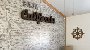 A living room with a grey sofa, wooden side table, and a wall with a distressed wood pattern and a 'California' sign. - Casa Tortugas - a Cozy, Relaxing House in a Gated Oceanfront Resort (Ensenada)