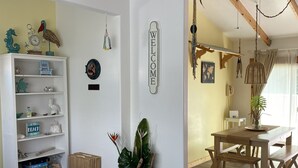 A room with a wooden dining table, a glass-top coffee table, a white bookshelf, and a 'WELCOME' sign on the wall. - Casa Tortugas - a Cozy, Relaxing House in a Gated Oceanfront Resort (Ensenada)