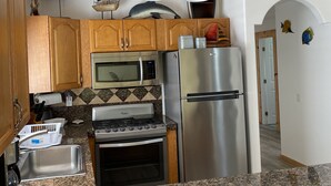 A kitchen with wooden cabinets, a stainless steel refrigerator, a microwave, and a stove. - Casa Tortugas - a Cozy, Relaxing House in a Gated Oceanfront Resort (Ensenada)