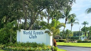 A sign for the World Tennis Club surrounded by lush greenery and palm trees. - Resort style vacation, 2BR/2BA condo in the heart of Naples: 8min to the beach (Naples)