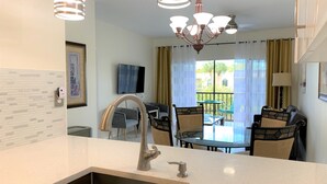 A modern kitchen with a stainless steel sink, a dining area with a glass table and chairs, and a chandelier. - Resort style vacation, 2BR/2BA condo in the heart of Naples: 8min to the beach (Naples)