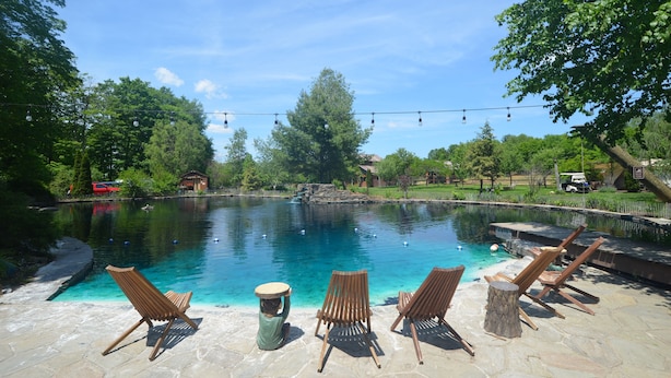 Une piscine à l’eau claire, entourée de carreaux de pierre et de chaises en bois.