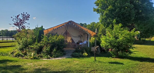 A small, rustic wooden structure with a pitched roof, surrounded by lush greenery and a clear sky.