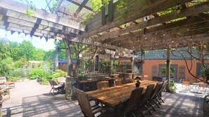 Une terrasse extérieure en bois, agrémentée d’une pergola, d’une table à manger avec des chaises et d’un petit coin bar.
