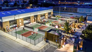 Un complexe sportif comprenant plusieurs courts de tennis, un espace de sièges couvert et un restaurant Chicken N Pickle.