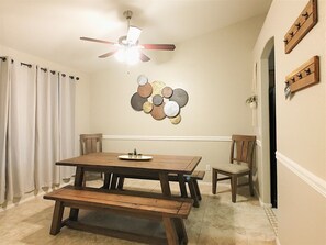 Un coin repas avec une table et des bancs en bois, un ventilateur de plafond et une composition décorative de plaques murales.