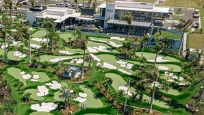 Un parcours de golf avec des bunkers de sable, des palmiers et un bâtiment en arrière-plan.