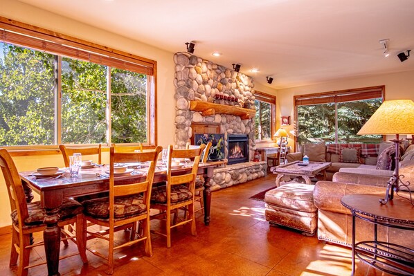 A dining area with a stone fireplace, wooden furniture, and large windows.