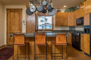 A kitchen with wooden cabinets, a central island with stools, a stove, and a microwave.