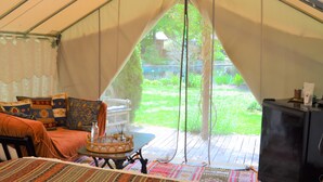 A tented room with a bed, a table with a basket, and a view of a grassy area outside.