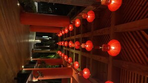 A corridor with red lanterns hanging from the ceiling, wooden pillars, and a view of a garden area. - Vidanta Luxury Paradise by (Nuevo Vallarta)