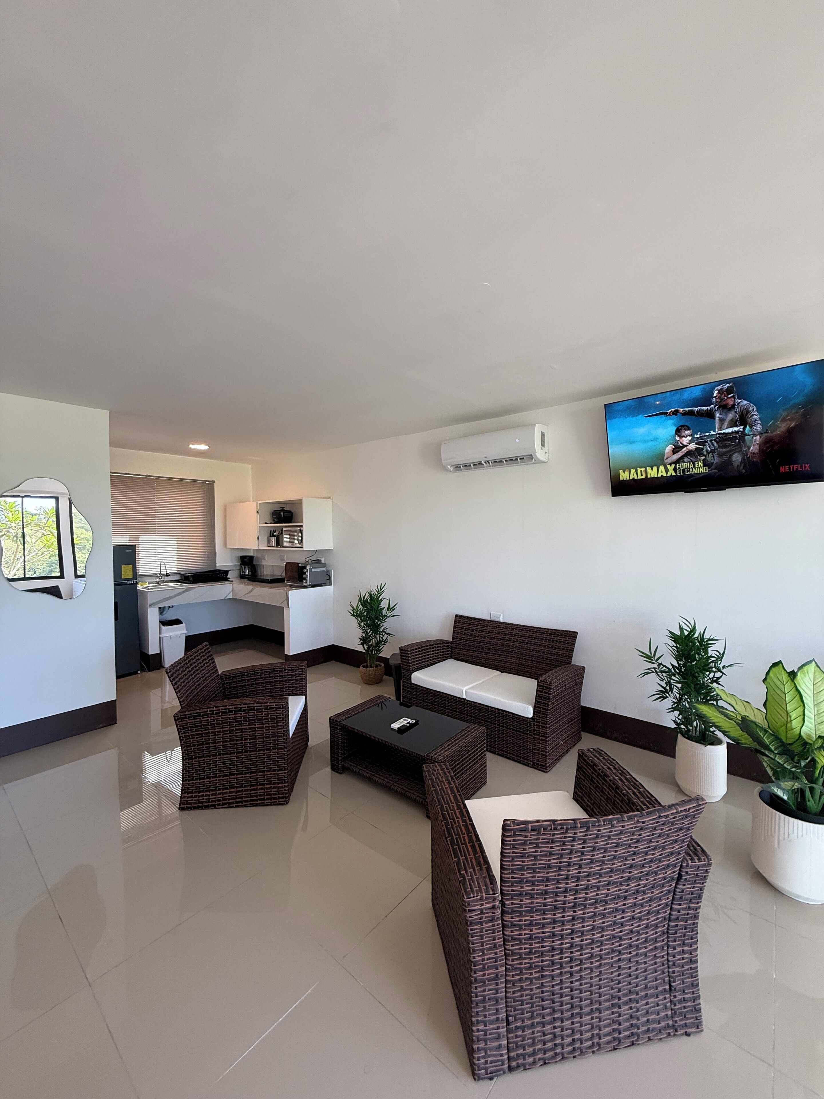 Una sala de estar moderna con muebles de mimbre, un televisor de pantalla plana y una cocina al fondo.