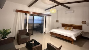 Une chambre à coucher avec un grand lit, un balcon avec des rideaux, des meubles en osier et un plafond avec des poutres apparentes.