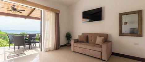 A living room with a sofa, TV, and a view of greenery through a large window.