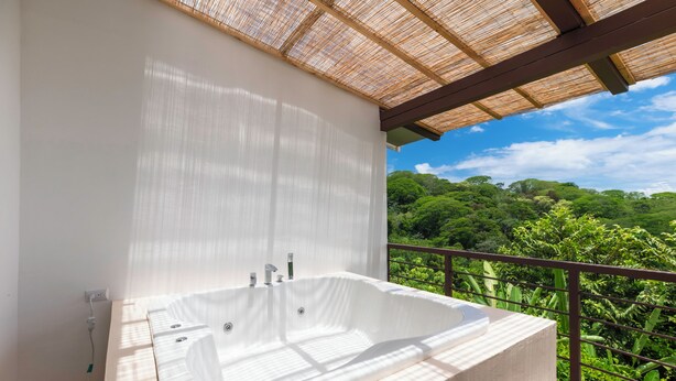 Une grande baignoire blanche, autoportante, installée sur un balcon offrant une vue sur une végétation luxuriante.