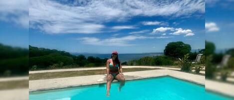 A person sitting by a pool with a clear sky and distant landscape.