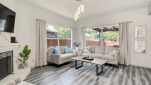 A spacious living room with a fireplace, two sofas, a coffee table, and a TV mounted on the wall. - Stylish House w playset ,Game room &BBQ near DFW airport ,Gaylord sleeps 10-14 (Flower Mound)