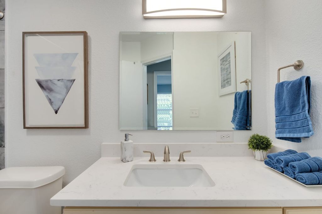 A bathroom with a white sink, three faucets, a framed artwork above the mirror, and blue towels on the wall.