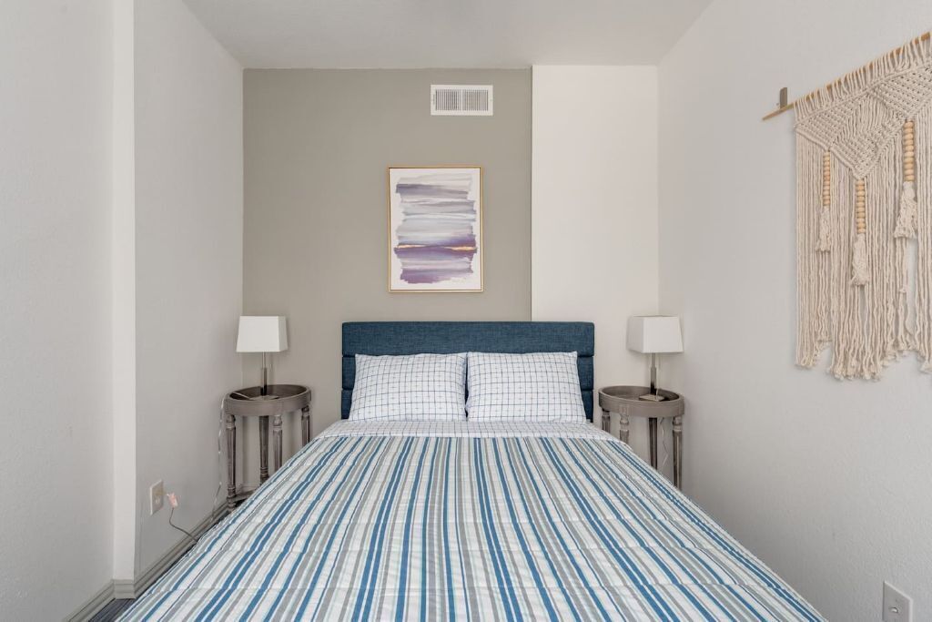 Ein Schlafzimmer mit einem Bett, zwei Nachttischen, einer Wanddekoration aus Makramee und einem gerahmten abstrakten Gemälde.