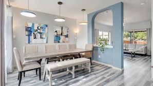 A dining area with a long table, benches, and hanging pendant lights. - Stylish House w playset ,Game room &BBQ near DFW airport ,Gaylord sleeps 10-14 (Flower Mound)